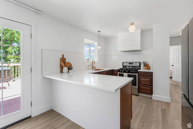 kitchen with stainless steel appliances, a peninsula, decorative backsplash, light wood-type flooring, and light countertops