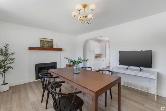 dining space featuring a fireplace, arched walkways, light wood-type flooring, and a chandelier