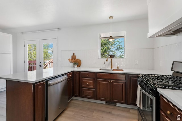 kitchen featuring appliances with stainless steel finishes, a peninsula, a sink, light countertops, and tasteful backsplash