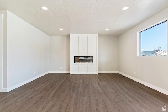 unfurnished living room with wood finished floors, recessed lighting, baseboards, and a glass covered fireplace