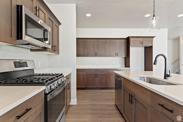 kitchen featuring stainless steel appliances, a sink, light wood-style flooring, light countertops, and hanging light fixtures