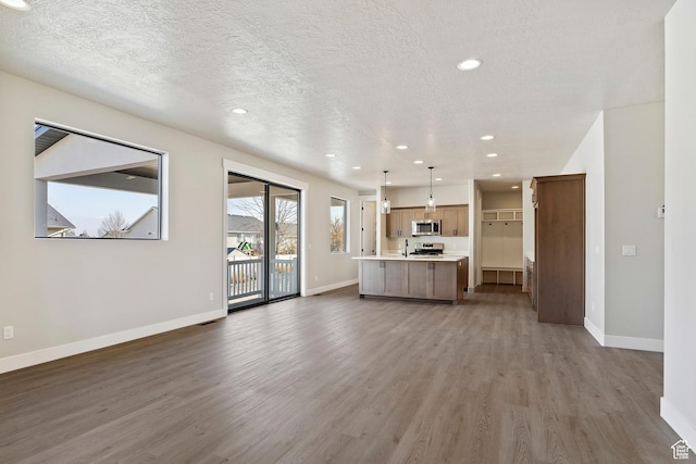 kitchen featuring stainless steel appliances, open floor plan, wood finished floors, light countertops, and baseboards