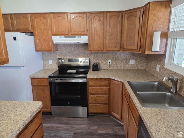 kitchen with under cabinet range hood, electric stove, freestanding refrigerator, a sink, and dark wood-style flooring