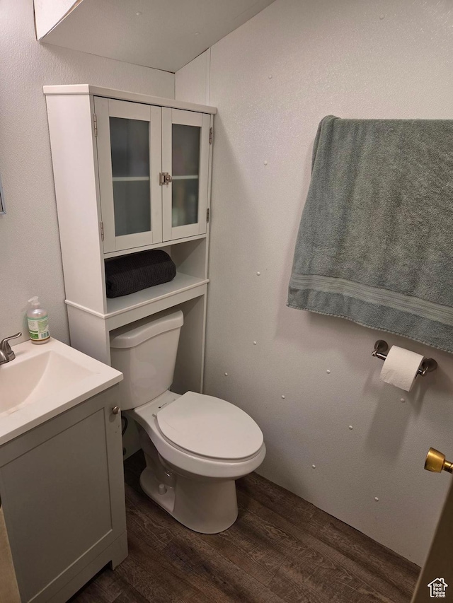 half bathroom with wood finished floors, toilet, and vanity