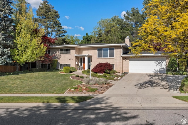 view of front of house with concrete driveway, brick siding, a front yard, a chimney, and a garage