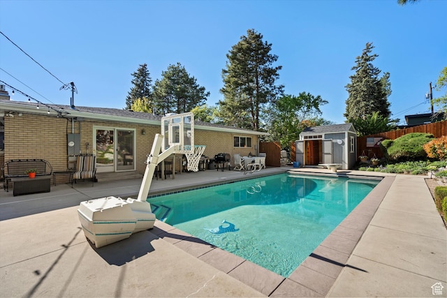 view of swimming pool featuring a patio area, a storage shed, a fenced backyard, an outbuilding, and a diving board