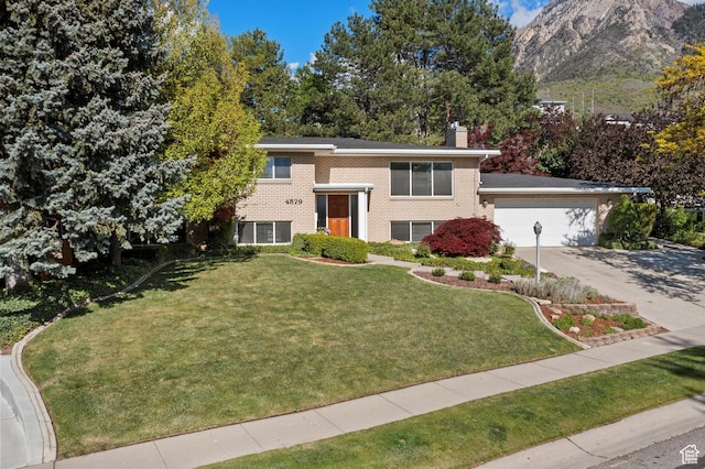 split foyer home featuring a chimney, brick siding, a front lawn, driveway, and an attached garage