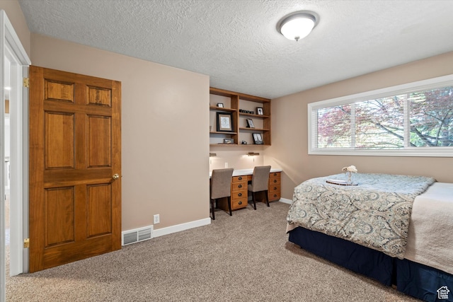 bedroom featuring light colored carpet, a textured ceiling, baseboards, and an office area