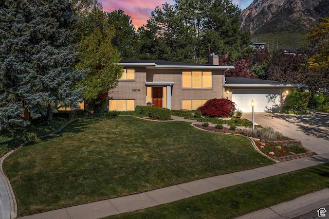 view of front facade featuring brick siding, a front yard, a chimney, driveway, and a garage