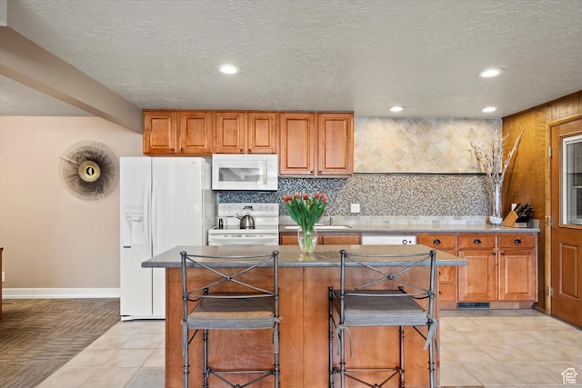 kitchen featuring white appliances, recessed lighting, brown cabinets, a breakfast bar area, and baseboards