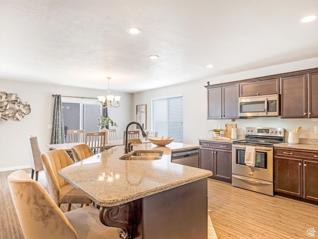 kitchen with appliances with stainless steel finishes, a sink, a chandelier, a kitchen island with sink, and a kitchen breakfast bar
