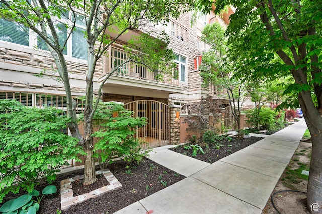 doorway to property featuring stone siding, a balcony, fence, and a gate