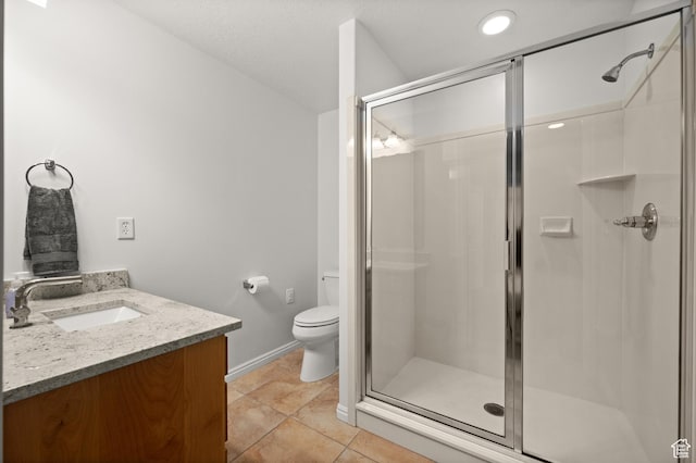 bathroom with a shower stall, toilet, vanity, baseboards, and tile patterned flooring