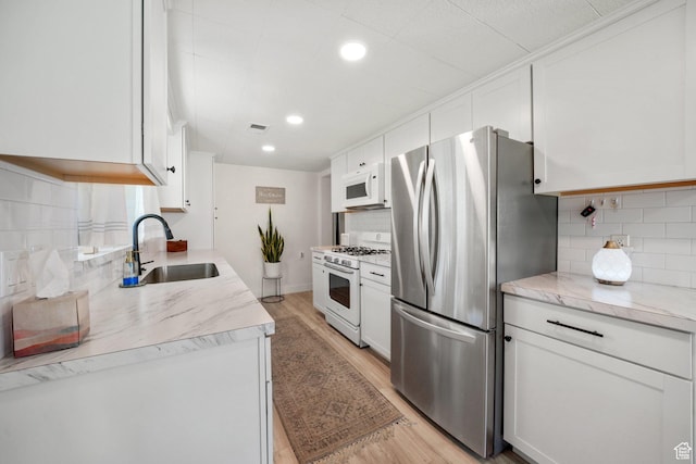 kitchen with white appliances, a sink, backsplash, white cabinets, and recessed lighting