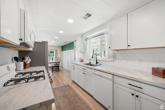 kitchen with a sink, white appliances, light wood-style floors, white cabinets, and healthy amount of natural light