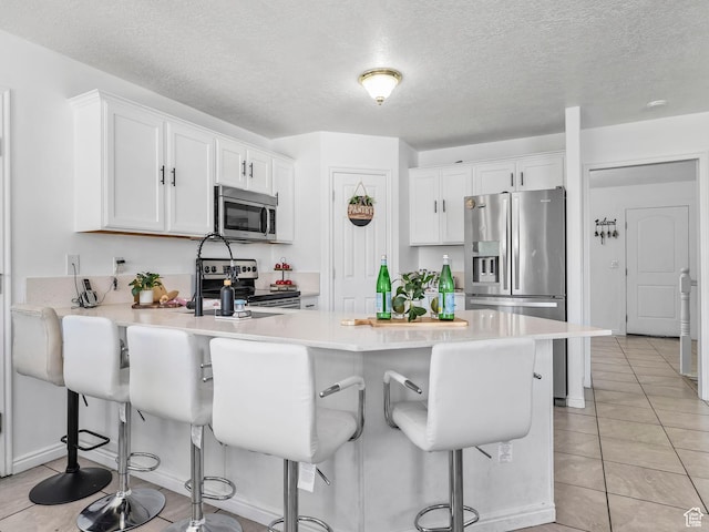 kitchen with stainless steel appliances, a peninsula, white cabinetry, light tile patterned floors, and a textured ceiling