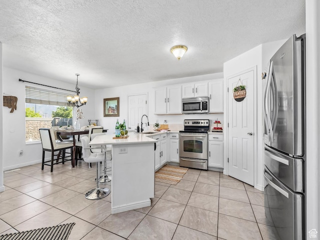 kitchen with stainless steel appliances, a peninsula, a sink, a chandelier, and white cabinets