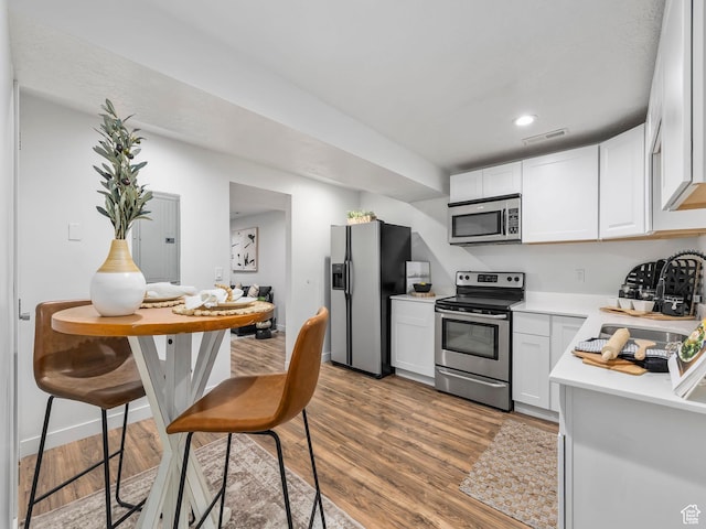 kitchen featuring stainless steel appliances, light countertops, wood finished floors, white cabinetry, and recessed lighting