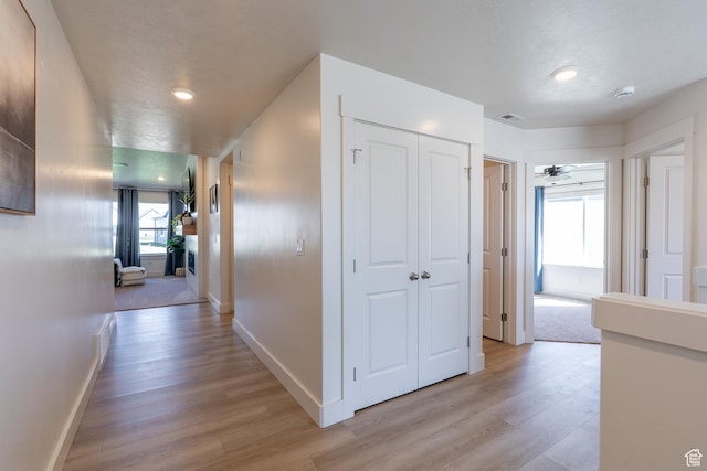 hallway featuring light wood-type flooring, baseboards, recessed lighting, and a textured ceiling