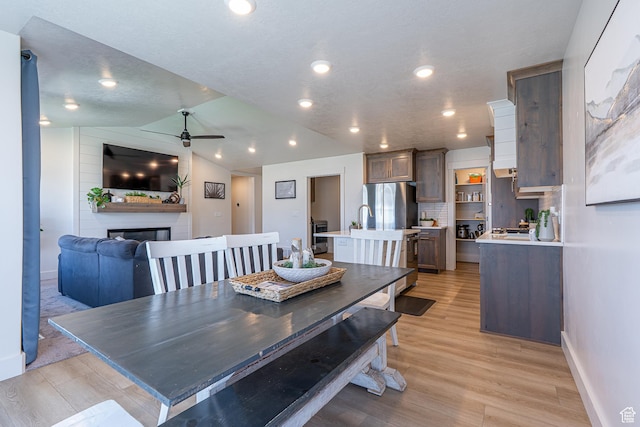 dining space featuring ceiling fan, light wood-type flooring, a large fireplace, baseboards, and recessed lighting