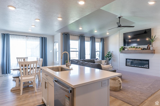 kitchen featuring a sink, open floor plan, light wood-type flooring, a large fireplace, and dishwasher