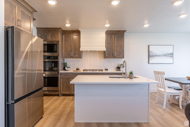 kitchen featuring appliances with stainless steel finishes, a sink, decorative backsplash, light countertops, and light wood-style floors