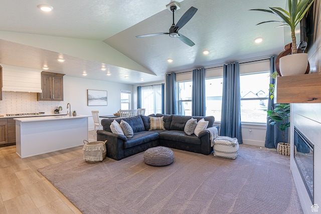 living room with ceiling fan, lofted ceiling, a glass covered fireplace, light wood-style flooring, and recessed lighting