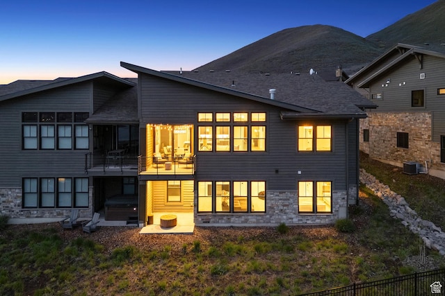 rear view of property featuring central air condition unit, stone siding, and a balcony