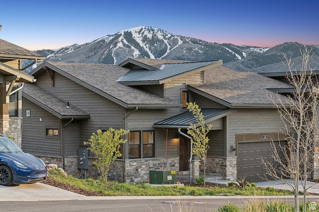 view of front of house featuring an attached garage, a mountain view, stone siding, a shingled roof, and driveway