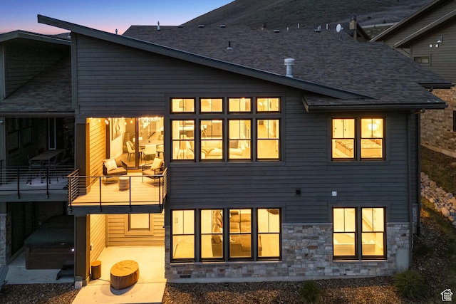 back of house at dusk with stone siding and a balcony