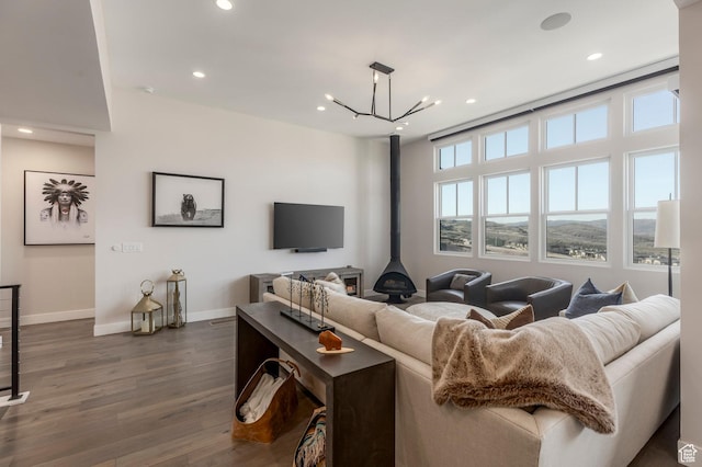 living room featuring dark wood-type flooring, baseboards, a wood stove, recessed lighting, and a chandelier