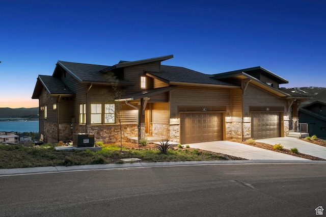 view of front of property with driveway, stone siding, an attached garage, and central AC unit