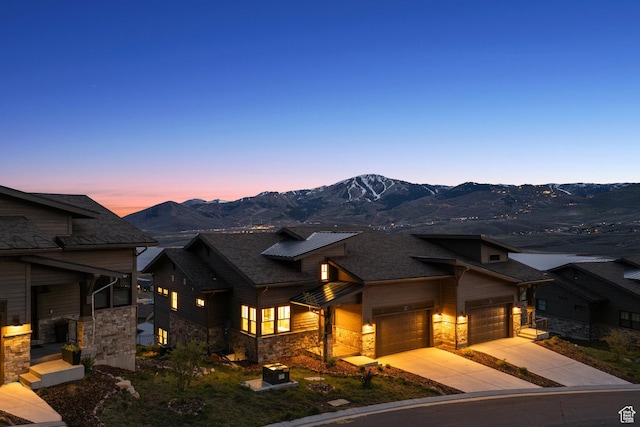 view of front of house with stone siding, a garage, concrete driveway, and a mountain view