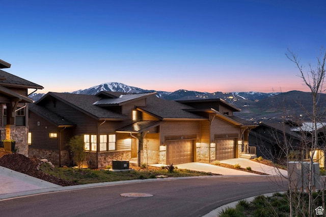 view of front of home with stone siding, concrete driveway, an attached garage, and a mountain view