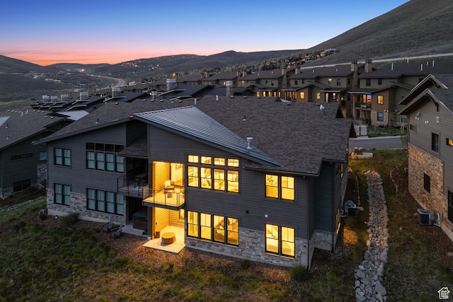 back of property at dusk featuring a mountain view, central AC unit, stone siding, and a residential view