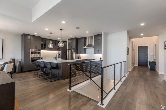 kitchen featuring wall chimney exhaust hood, stainless steel appliances, a breakfast bar, recessed lighting, and light wood-style floors