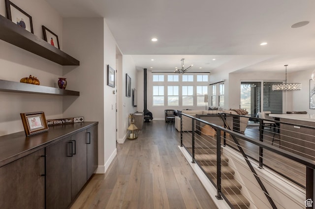 hallway featuring a chandelier, baseboards, light wood finished floors, recessed lighting, and an upstairs landing