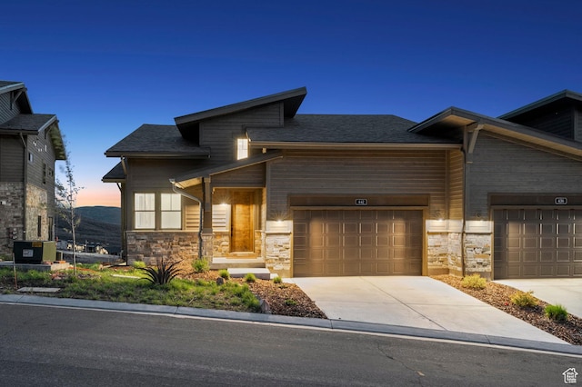 view of front of property featuring stone siding, driveway, a garage, and roof with shingles
