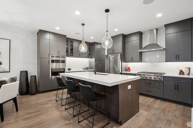kitchen with stainless steel appliances, wall chimney exhaust hood, a sink, light countertops, and light wood-style flooring