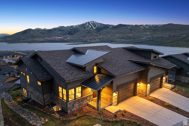 view of front of house with stone siding, roof with shingles, a garage, concrete driveway, and a water and mountain view