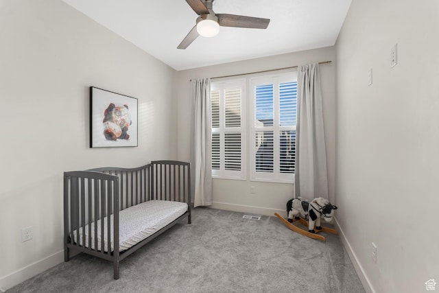 carpeted bedroom featuring baseboards, a crib, and ceiling fan