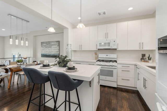 kitchen featuring white appliances, a kitchen bar, dark wood-style flooring, light countertops, and hanging light fixtures