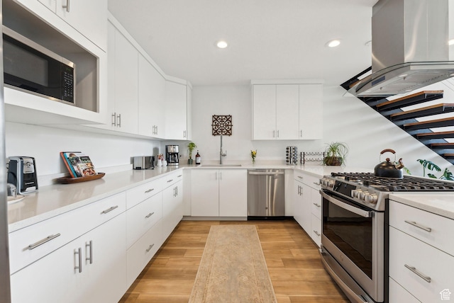 kitchen featuring appliances with stainless steel finishes, island exhaust hood, a sink, light countertops, and light wood-style floors
