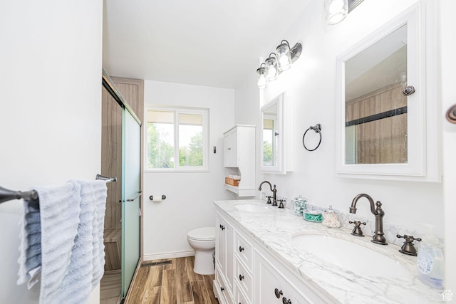 full bath with double vanity, toilet, an enclosed shower, wood finished floors, and baseboards