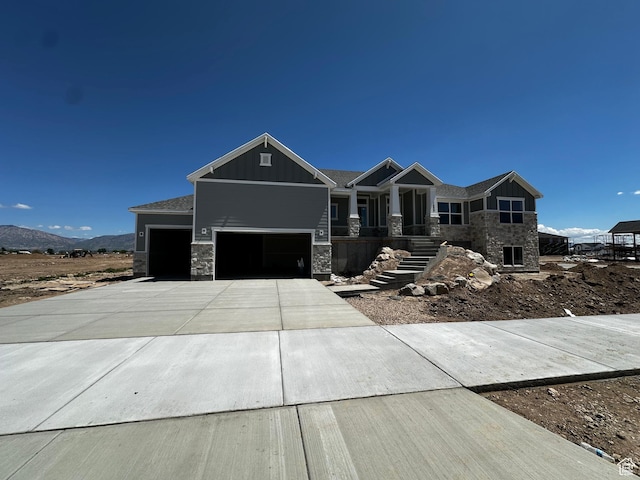 craftsman house with an attached garage, board and batten siding, stone siding, driveway, and a mountain view