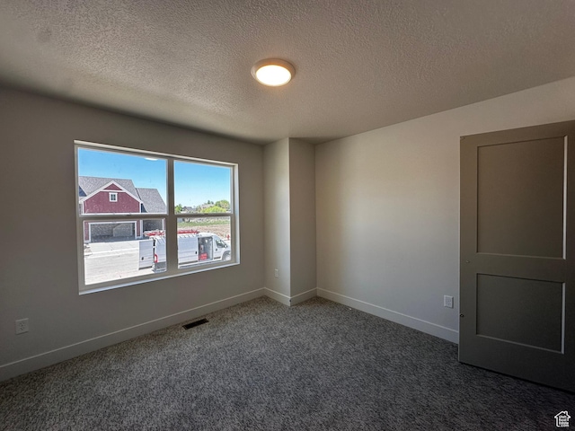 spare room featuring a textured ceiling, dark carpet, and baseboards