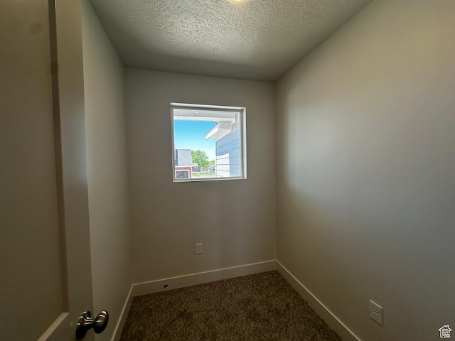 empty room with baseboards, dark carpet, and a textured ceiling