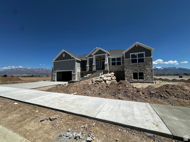 view of front facade featuring stone siding, board and batten siding, an attached garage, a mountain view, and driveway
