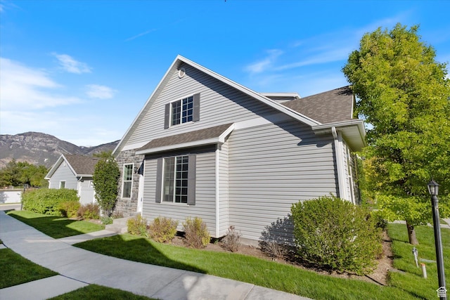 view of side of home with a lawn, a mountain view, and a shingled roof