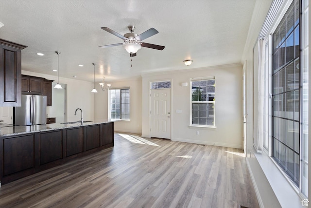 kitchen featuring freestanding refrigerator, a sink, dark brown cabinetry, wood finished floors, and crown molding